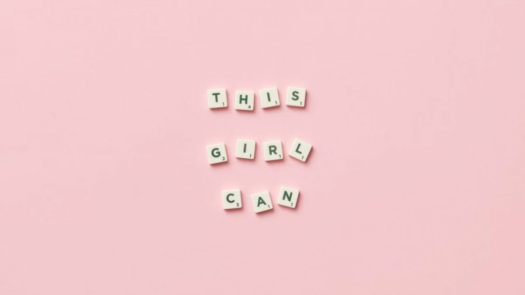 Scrabble tiles spelling 'This Girl Can' on a pink background.